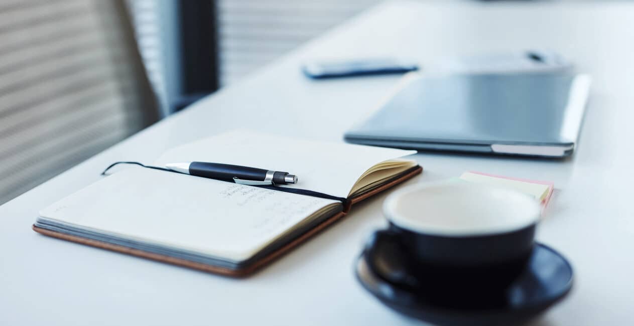 a journal with a pen and a coffee mug on a white table