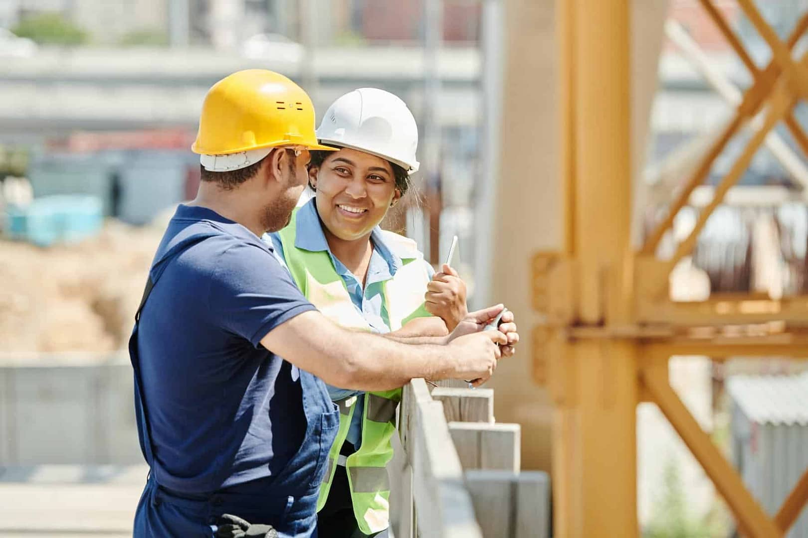 Two construction workers discuss stand on scaffolding while smiling