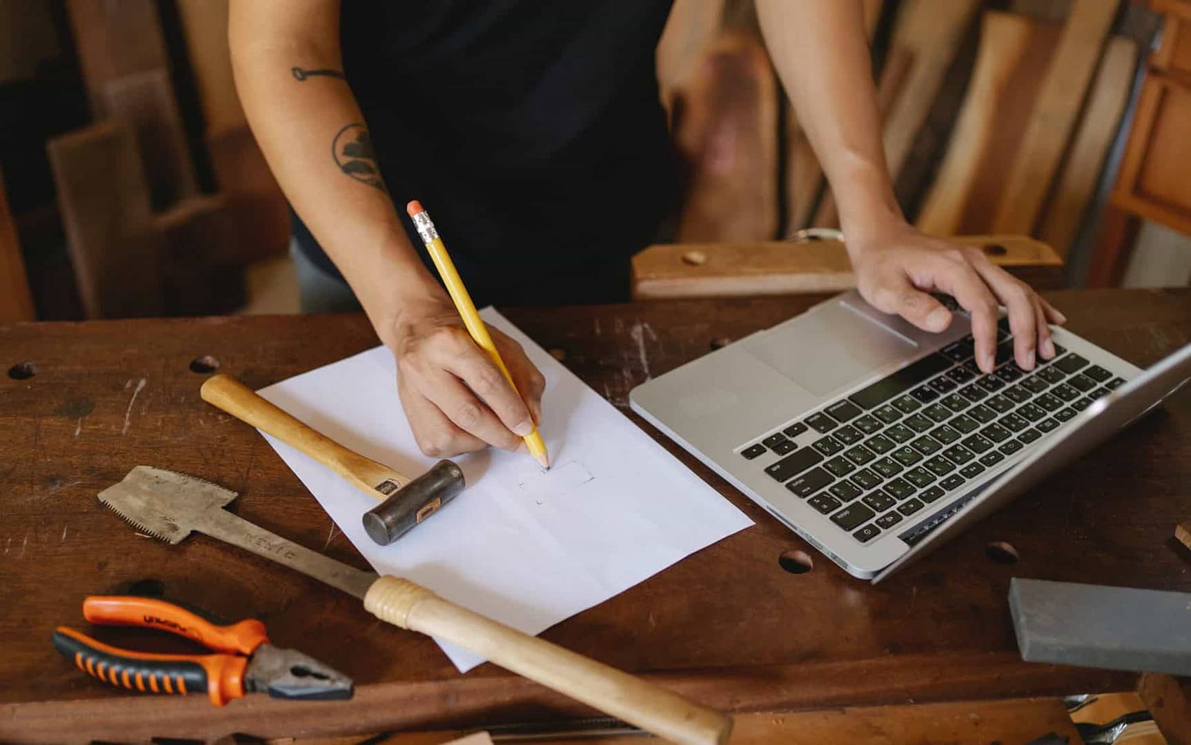 Construction worker writes on paper while researching on laptop with tools around him