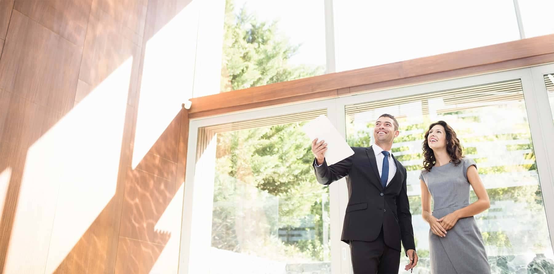 A real estate agent showing a client a house with floor to ceiling windows.