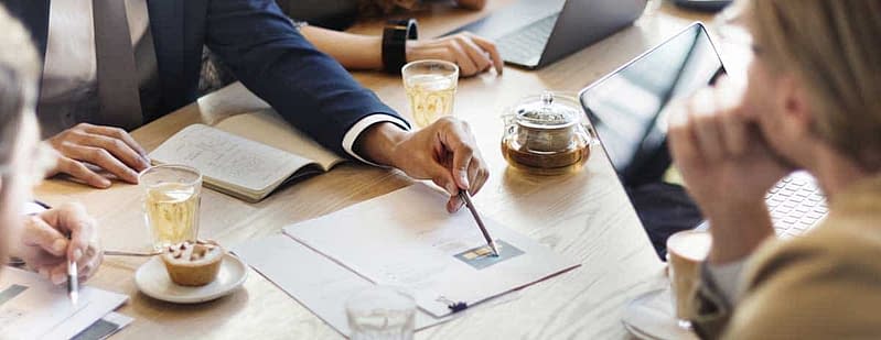 Corporate Retirement Planning Advisors sit a wooden table and are pointing at a paper report with a back pen
