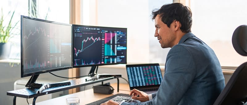 Man in suit looking at computer monitor screen of stock market in daylight
