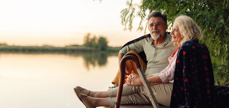 Elderly couple relaxing on a pier, sharing a blanket and enjoying the sunset over the lake