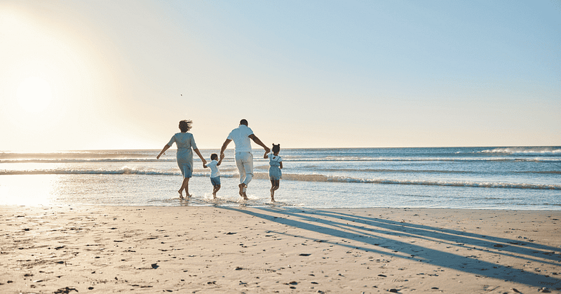 Family running on beach in the sunlight hands locked running towards ocean
