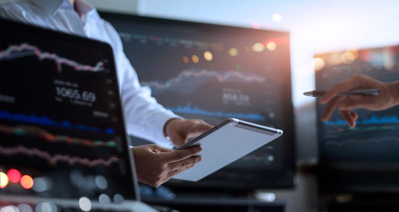 Business team working together. Businessman using tablet for analyzing data stock market in monitoring room with team pointing on the data presented in the chart on screen, forex trading graph, stock exchange trading online, financial investment concept, which Aldrich Wealth provides assistance to clients on. All on laptop screen are design up.