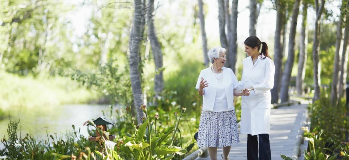 A doctor walking through a wooded pathway with an elderly lady.