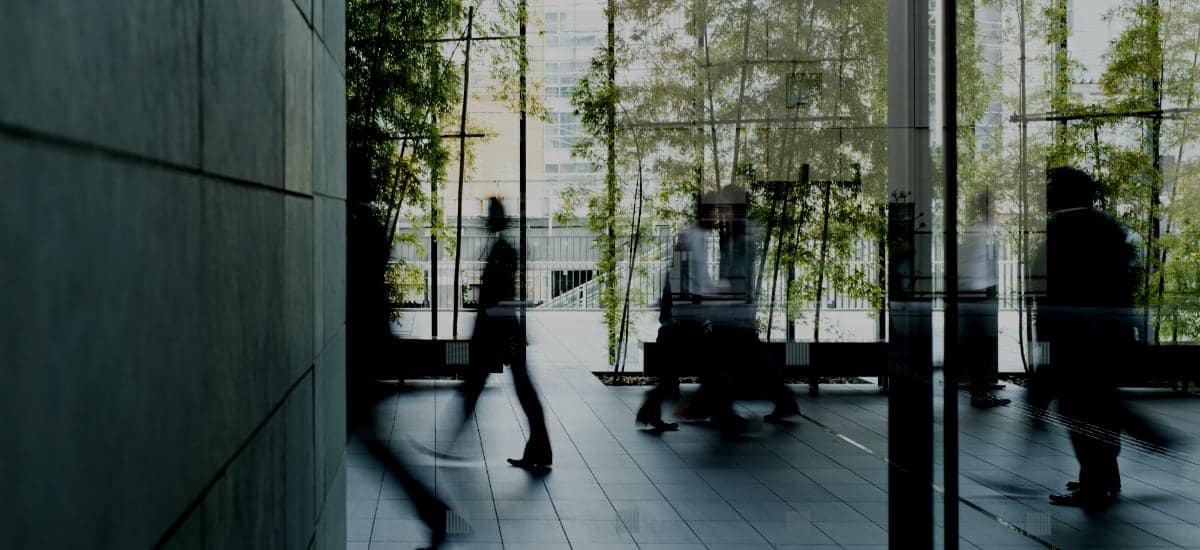 Blurs of people walking through an office lobby space with lots of greenery.