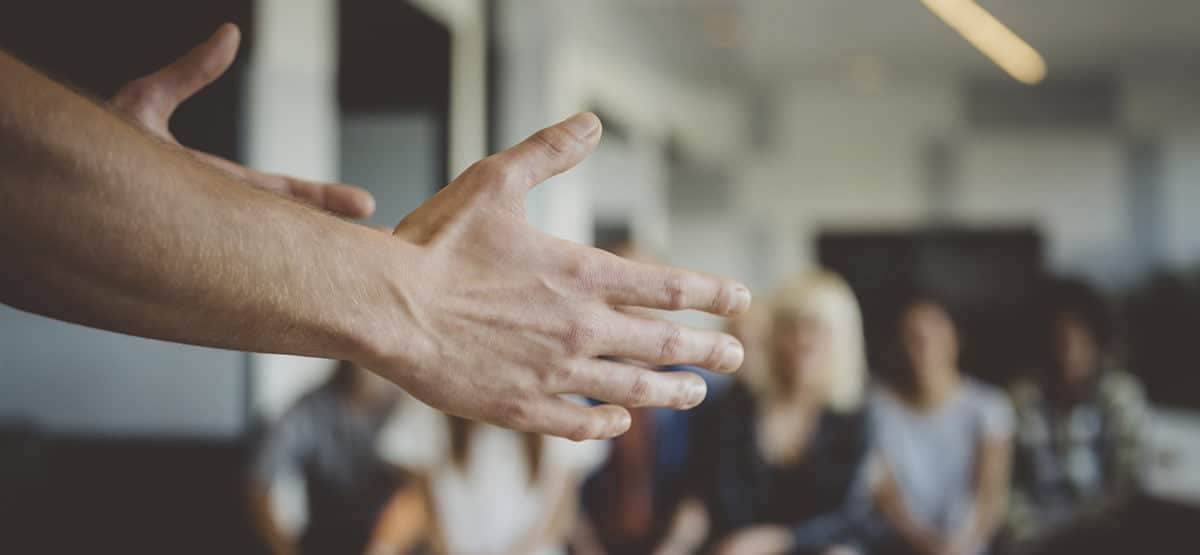 A view of a person's hands while they are speaking to an audience of blurred figures.