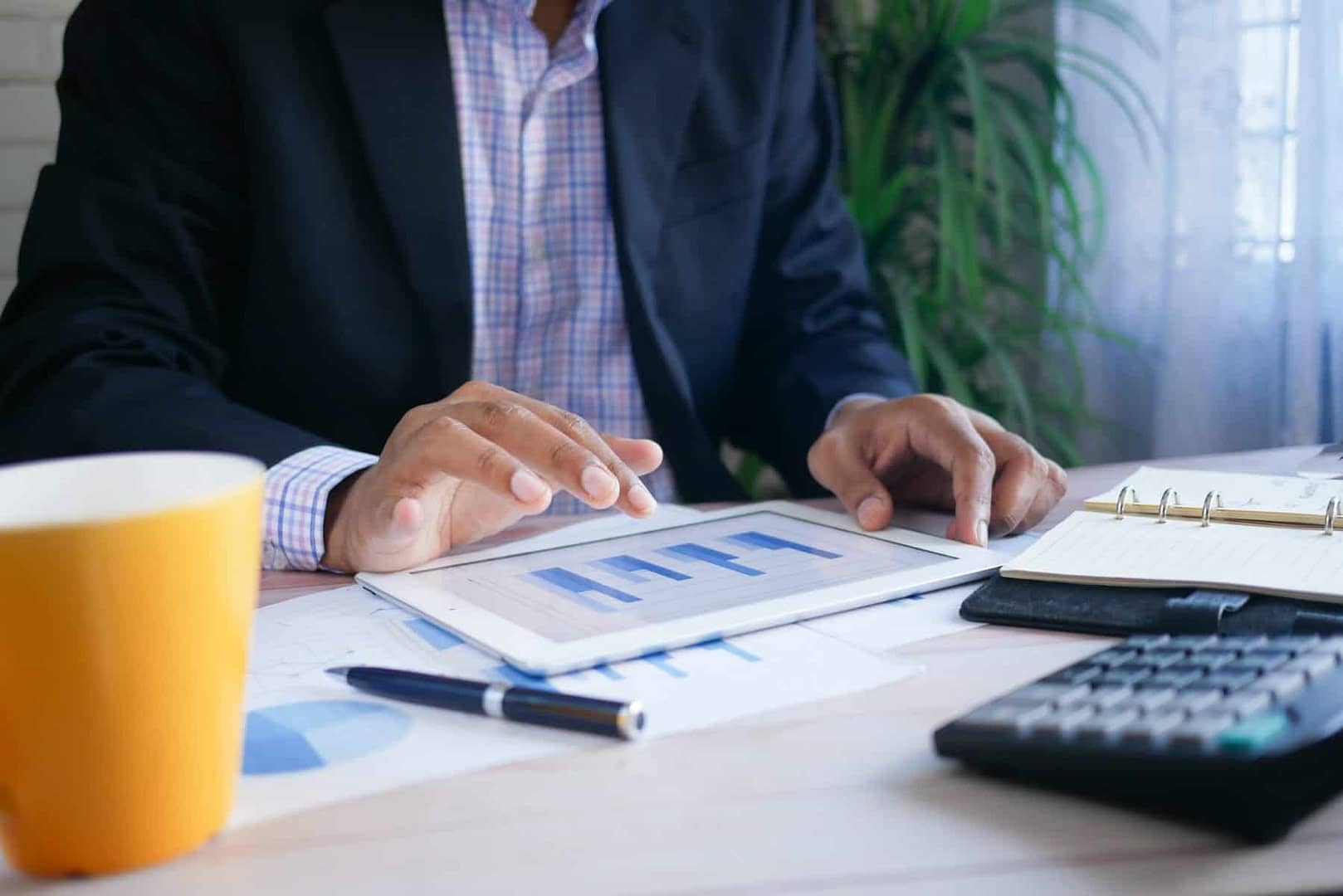 A nonprofit auditor reviews financial statements with a tablet, calculator, and cup of coffee.