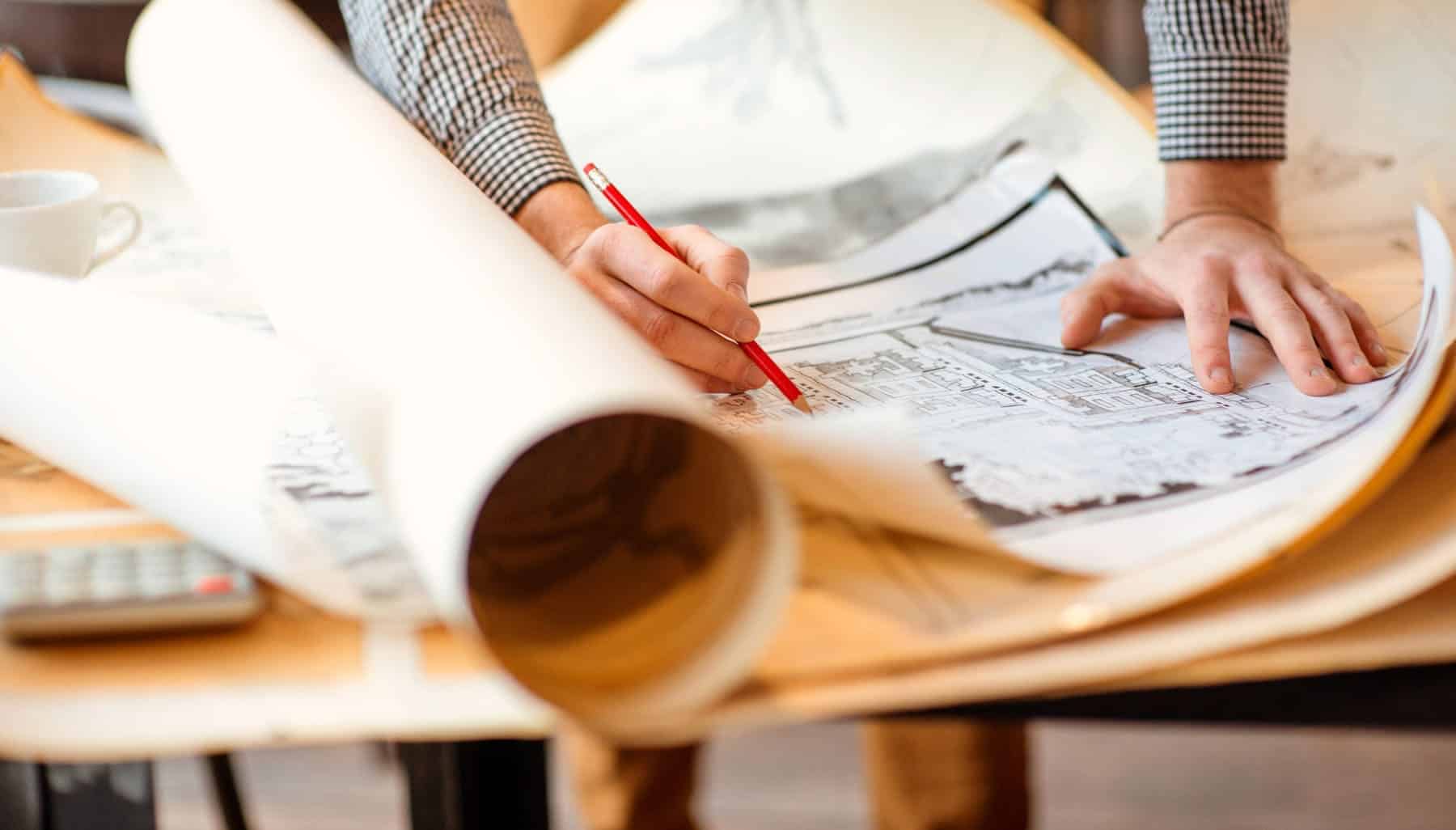 A person’s hand holding a pencil making changes to a blueprint that will take advantage of R&D construction tax credits