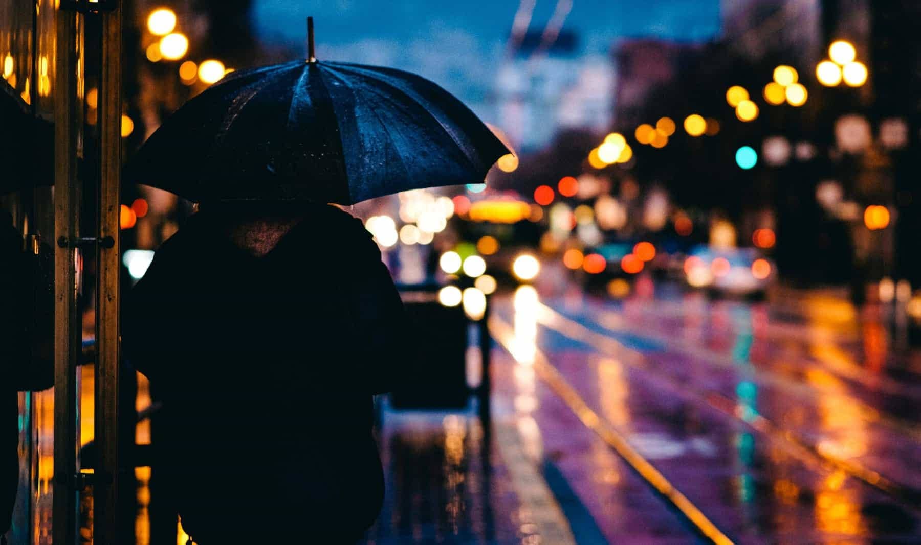 woman stands on street with umbrella