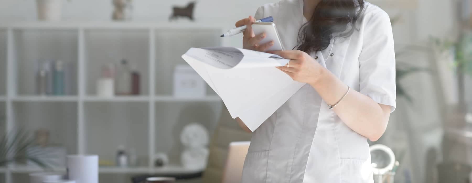 A doctor writing on some papers in a white office space.