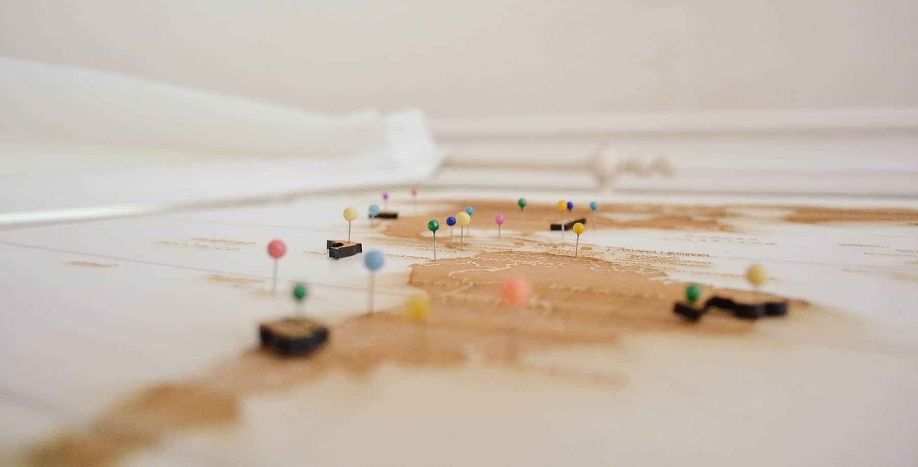 A view of a map on a wall with thumbtacks marking cities and locations.