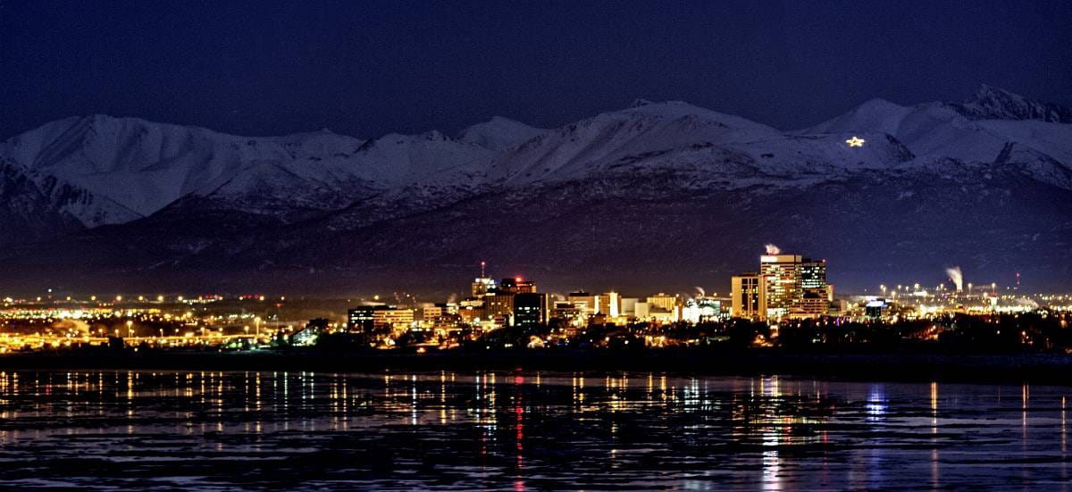 A picture of the lit city and snowy mountains of Anchorage at night, where Aldrich Advisors offers audit and assurance, business advisory, employee benefits, private client, retirement planning, tax planning, technology, and wealth management services in Anchorage and all throughout Alaska.