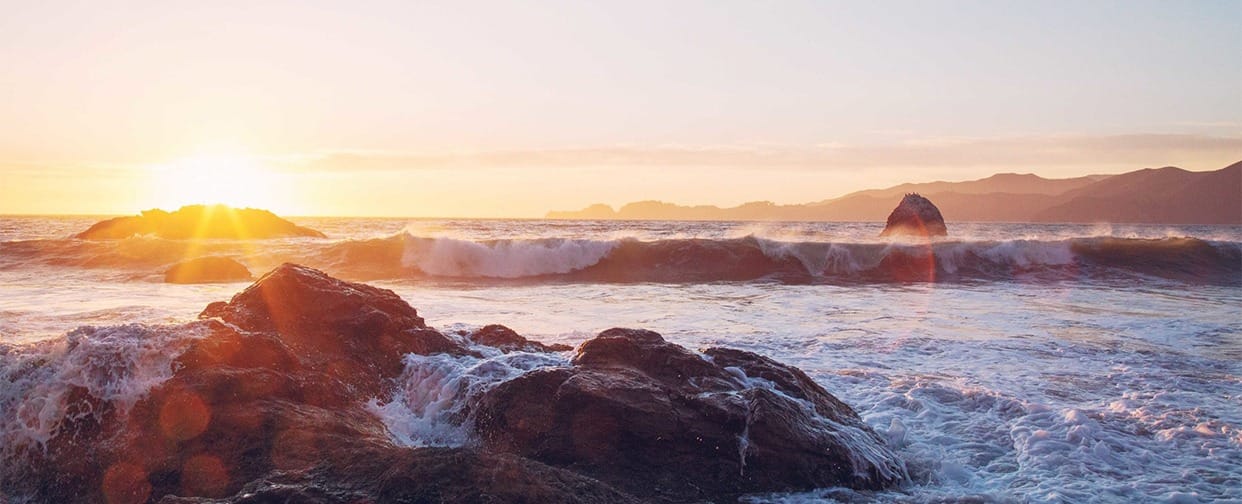 A rolling wave approaching a rocky shore under a golden sunset