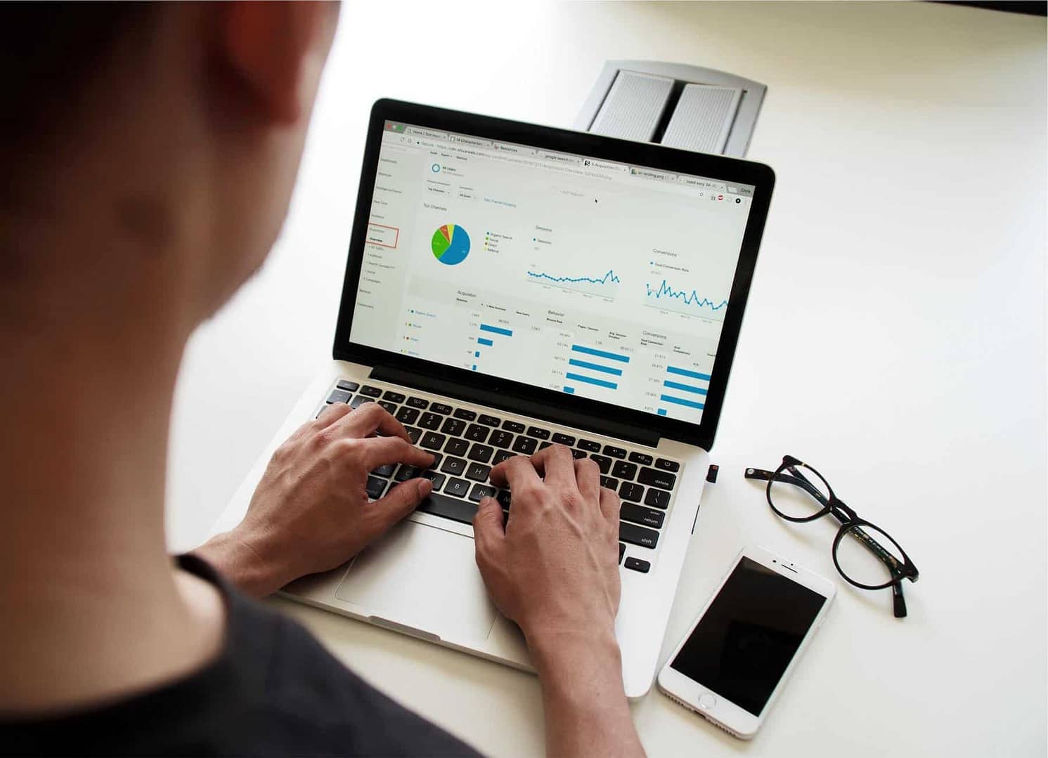 A person looking at Google Analytics on their laptop with their phone and glasses to their right in the