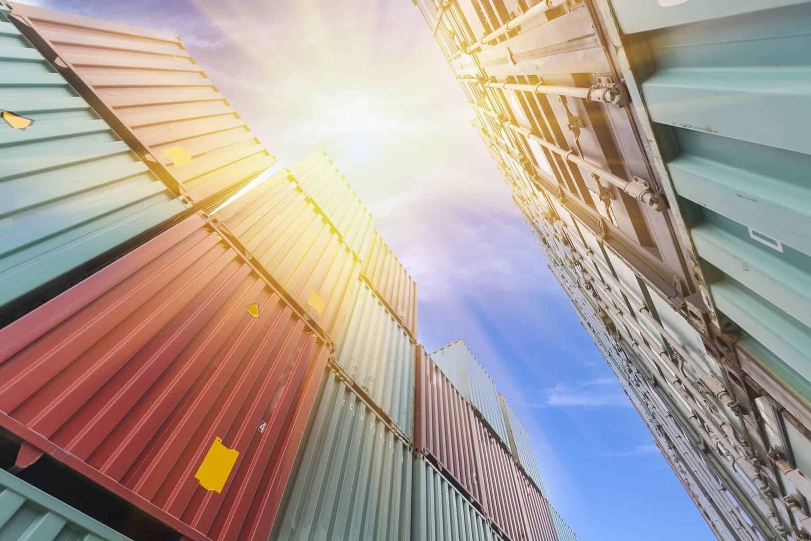 An image looking up at a blue sunny sky with blue and red shipping containers stacked on each side.