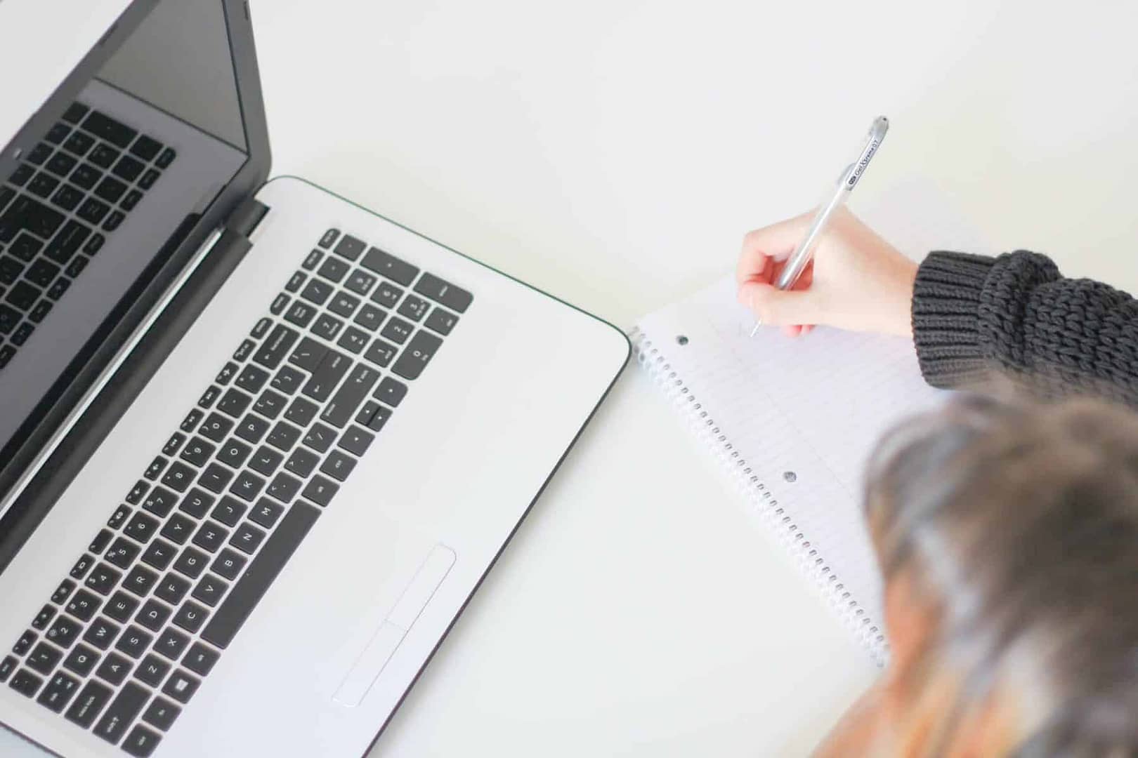 White desk with a laptop and a person writing on a piece of paper