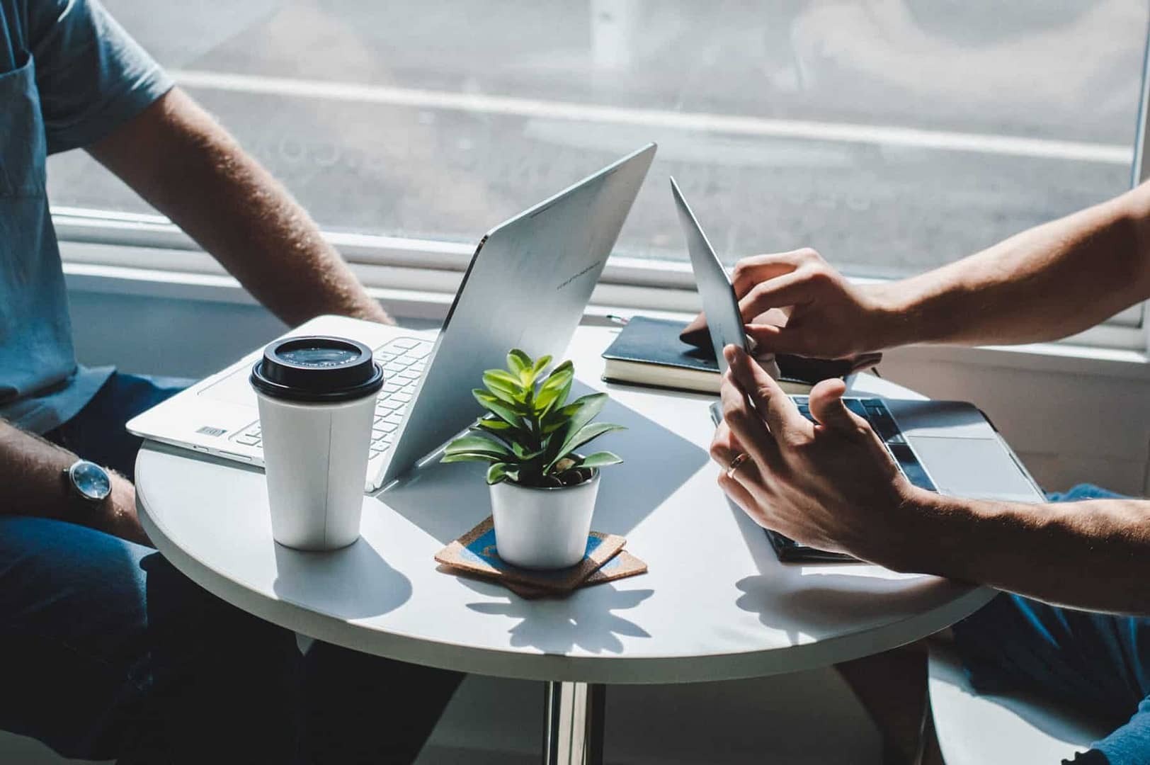 Two businessmen sit at a cafe table with a small plant to discuss M&A Activity in Q2 2022