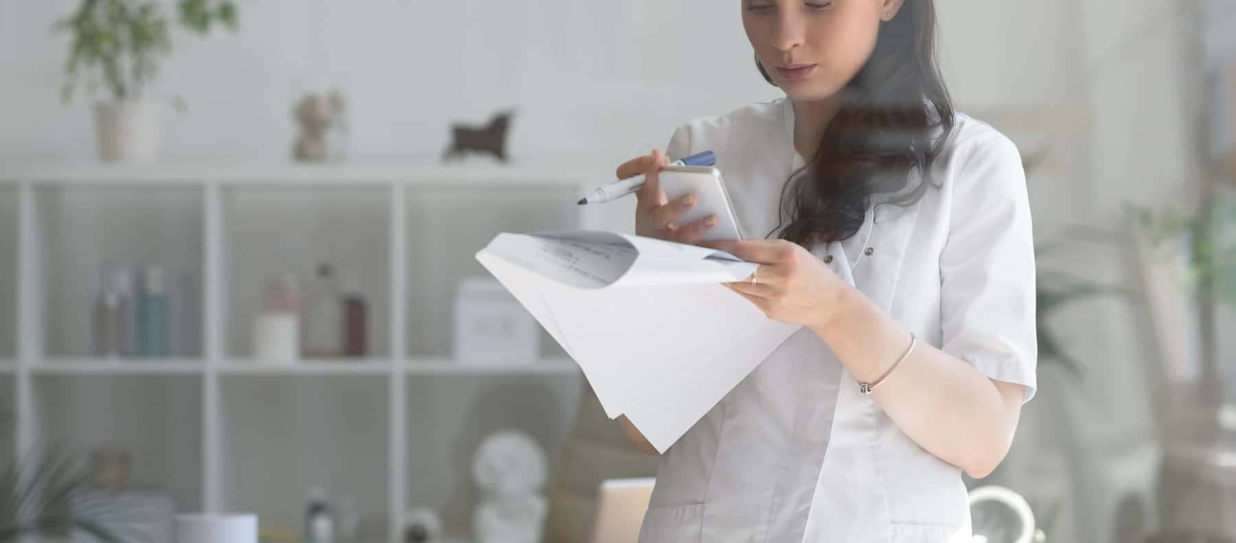 A doctor writing on some papers in a white office space.