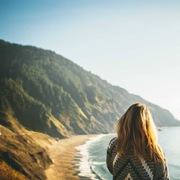 A person facing the opposite direction standing from a high area overlooking a beach stretching into the distance