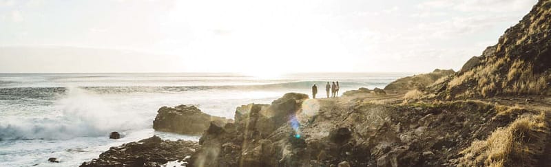 People gathering around a cliff and admiring the view of the ocean, waves, rocks, and sunset