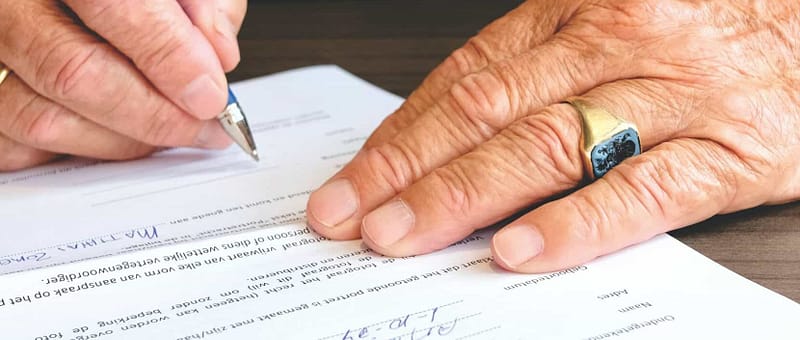 person signing paperwork by hand with blue pen