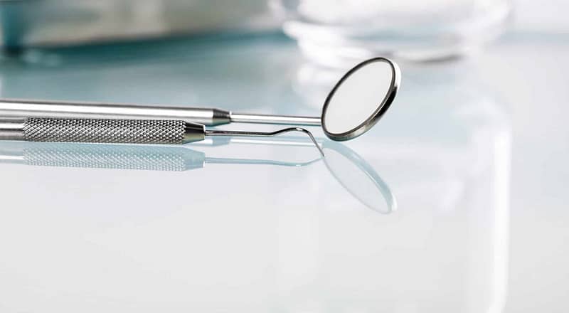 A metal mirror and pick dental instrument on a glass reflective table.