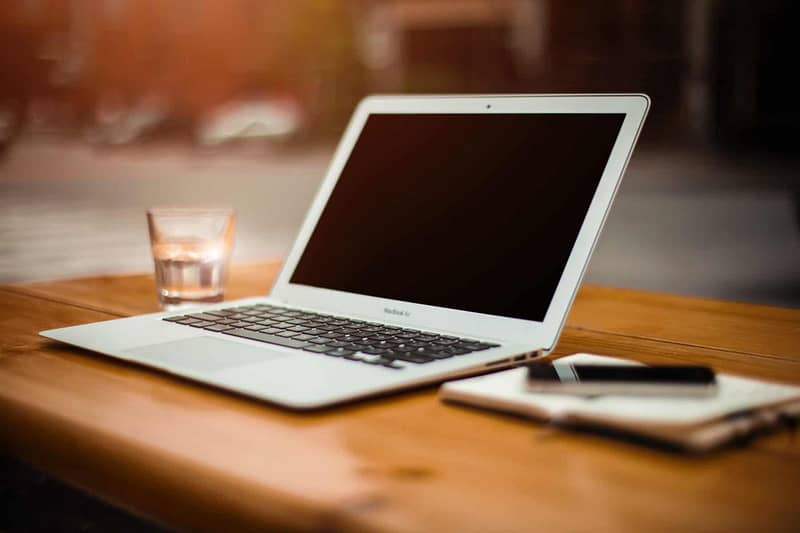 laptop sits on desk with a glass of water and a pad of paper