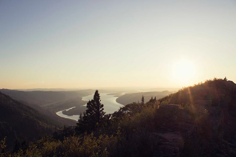 Overlooking tree covered hills with a wide river in the distance at dusk.