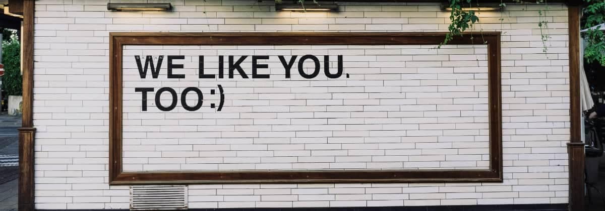 An image with a white brick wall with a sign that says "We like you too" with a smiley face.