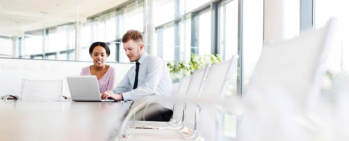 A business valuation advisor and a client sit at a table in a brightly lit room with a laptop.