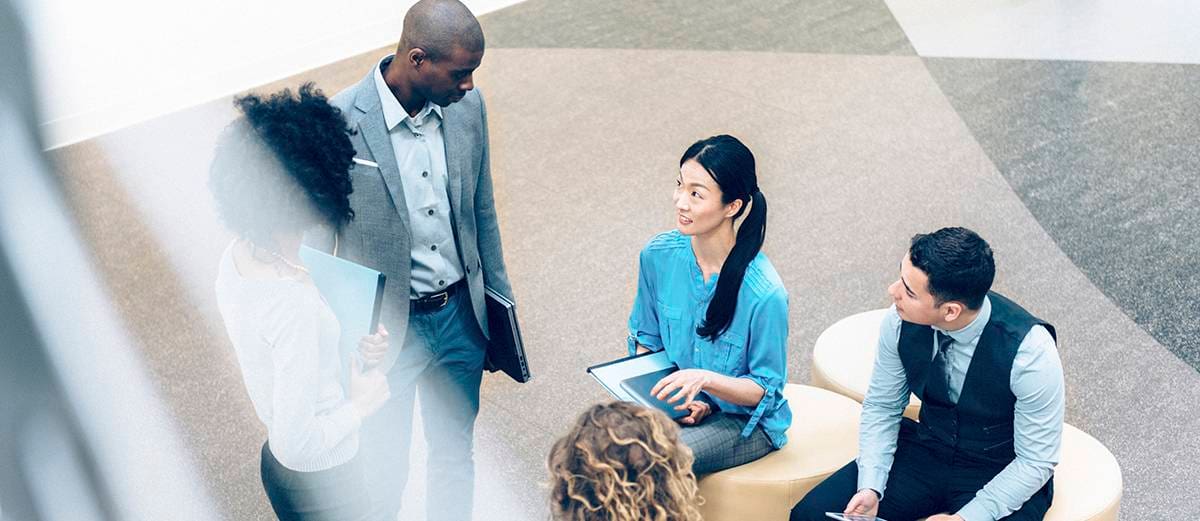 Overhead view of three business advisors assisting a client with a transaction in a wide open, indoor space.