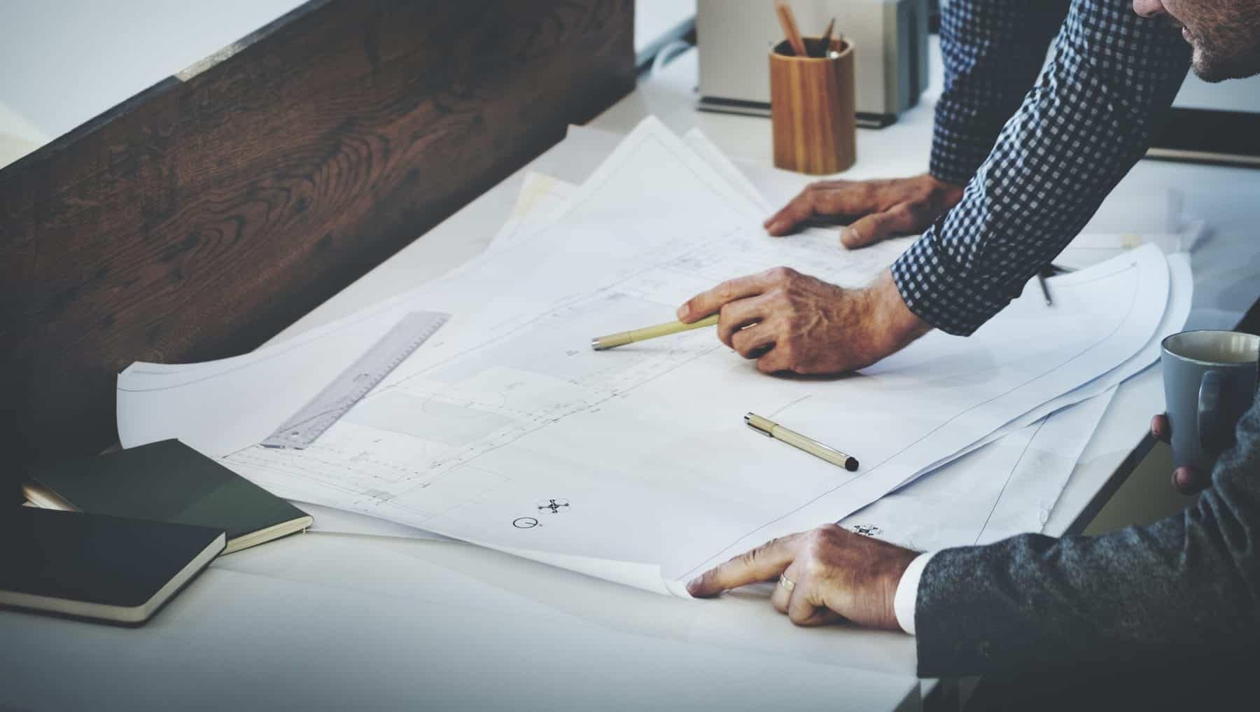The hands of an accountant with a pencil pointing at details on an architecture and engineering firm’s blueprint.