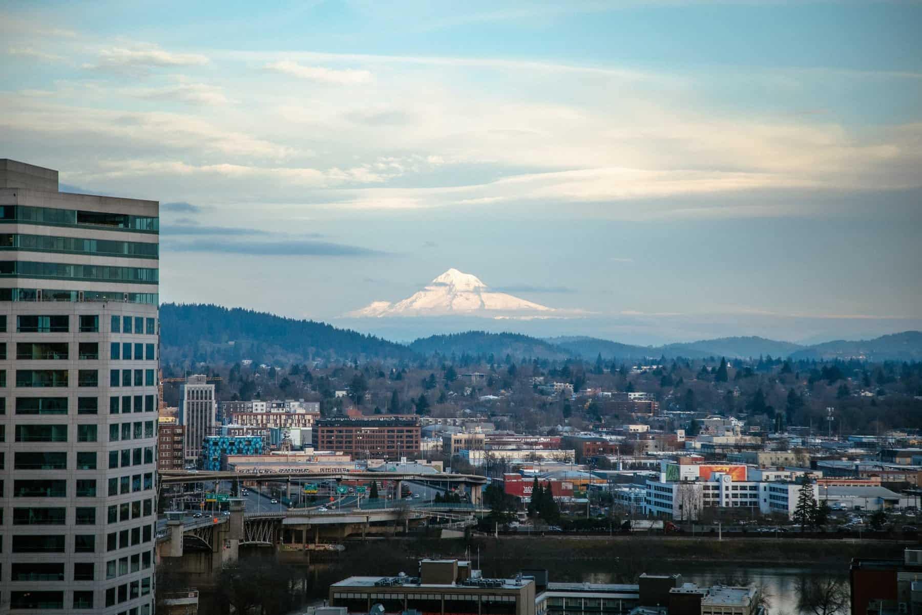 Cityscape of Portland, OR with skyscrapers and a mountain view in the background on a partly cloudy day