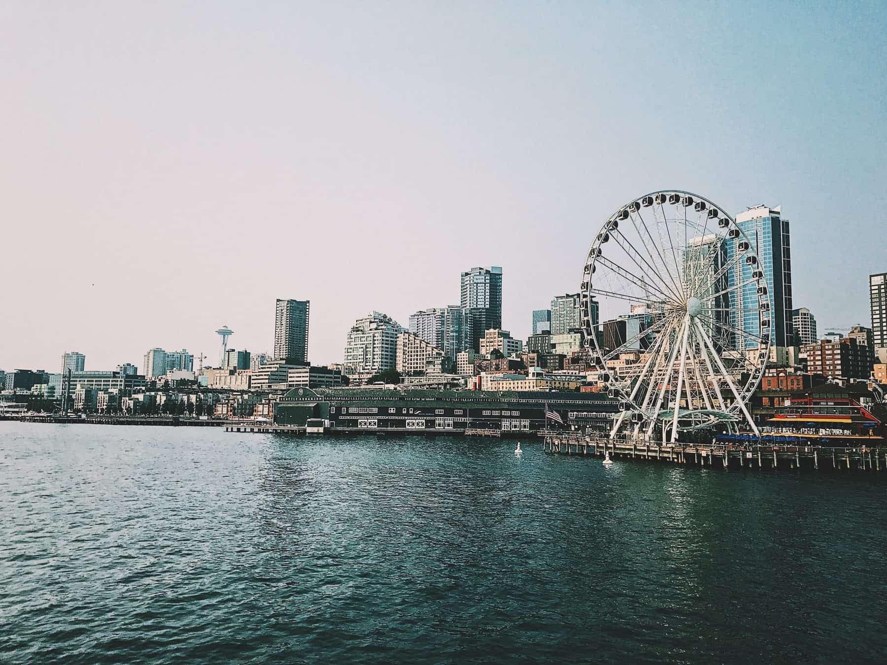 The skyline of Seattle showing the water, space needle in the background, and the Seattle Ferris Wheel. Washington locals should be aware of the new Washington state capital gains tax for individuals who have Washington allocated gains.