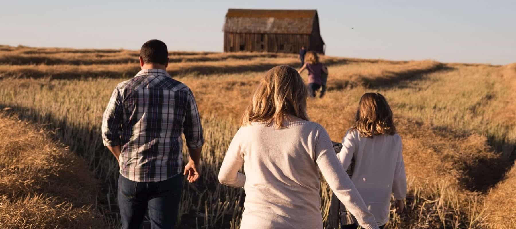 A photo of a man and two female children walking down a path on a farm with a barn in the background.