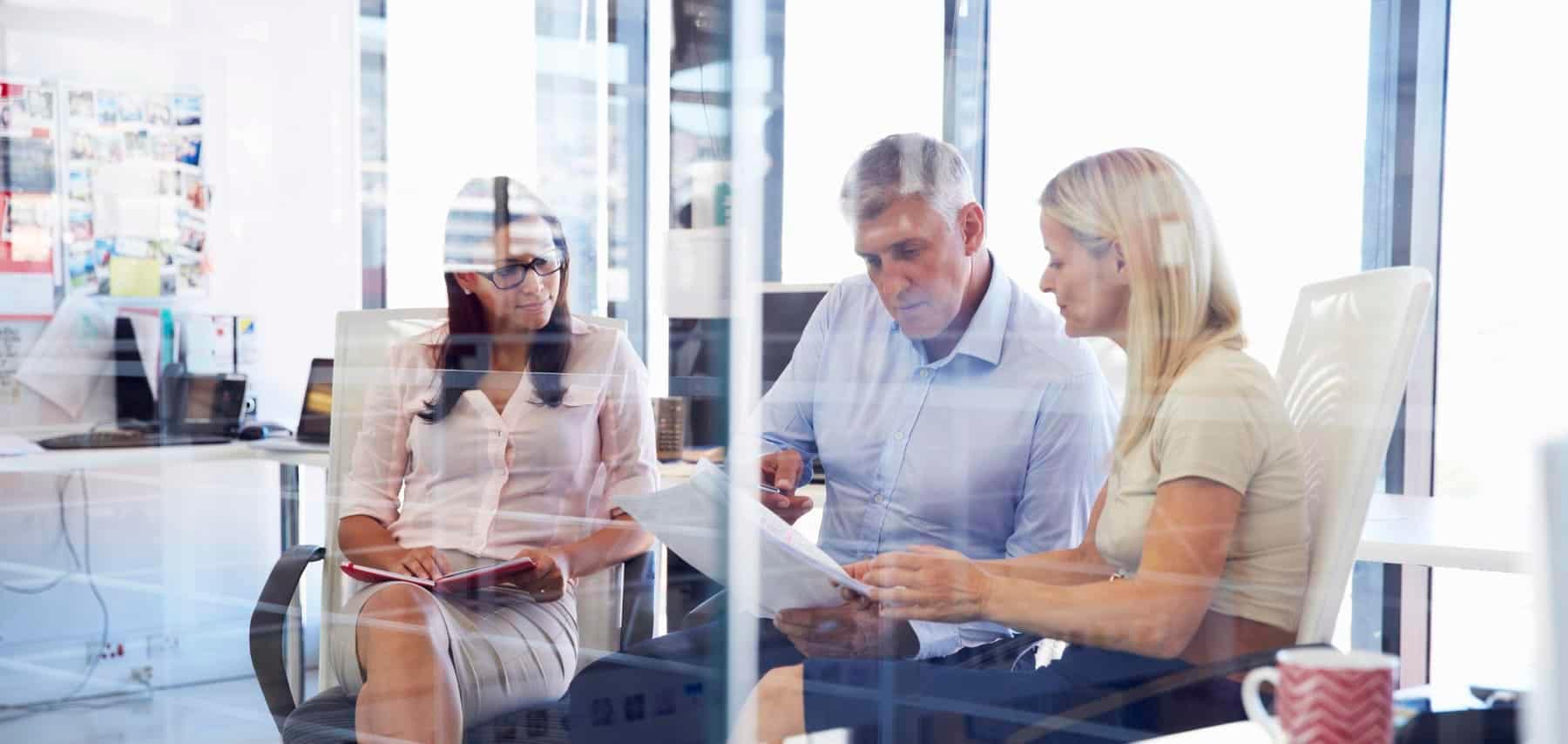 Two certified succession planners and a client in a brightly lit office working on a transition plan.