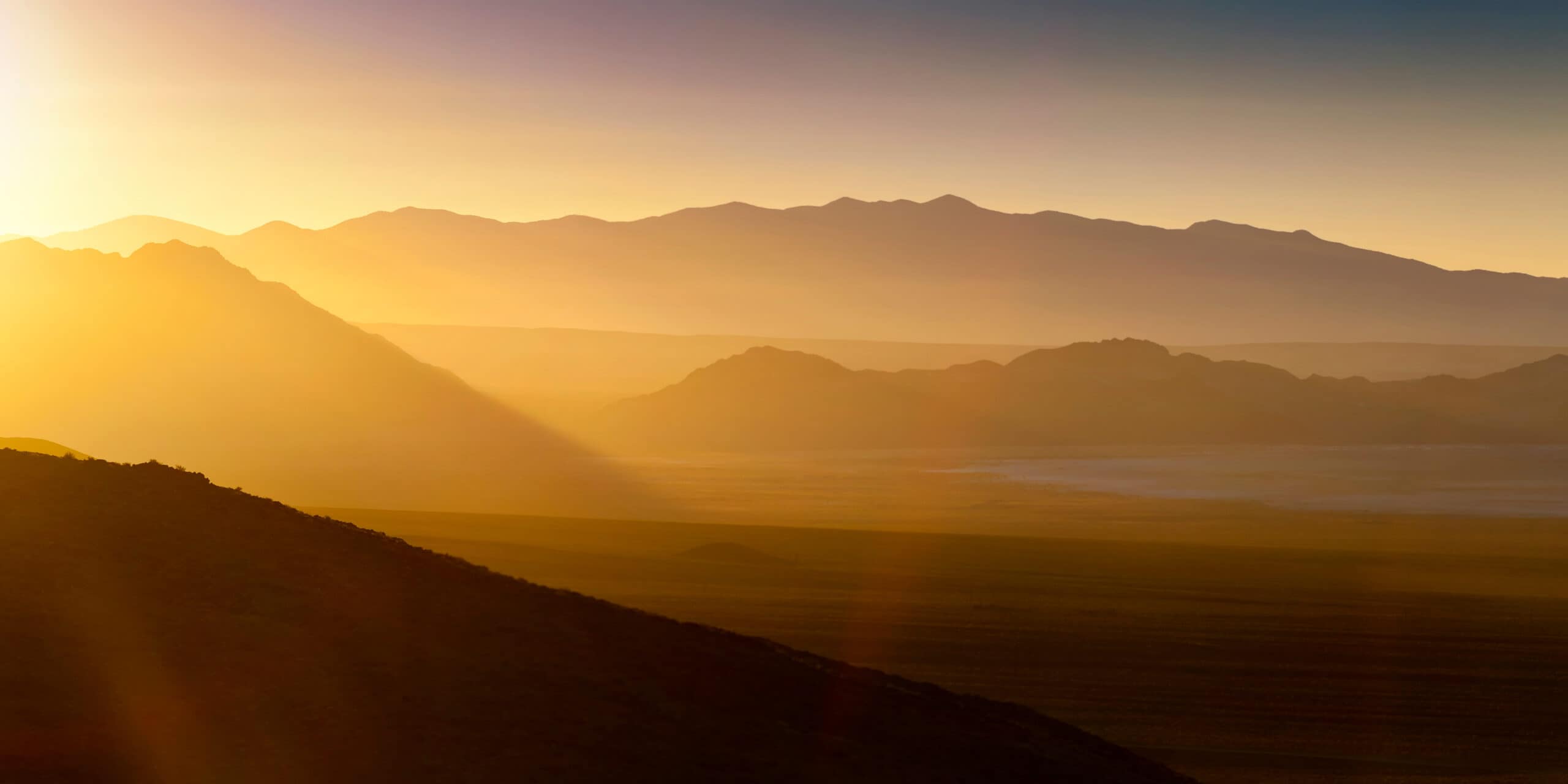 Yellow sunset over three mountain ranges from a bird's-eye view.