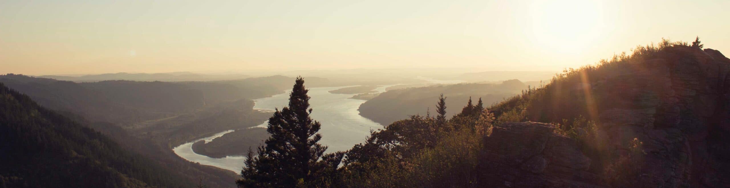 Overlooking tree covered hills with a wide river in the distance at dusk.