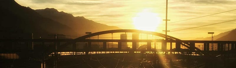 Sunset view of a railroad in an industrial area with a bridge off in the distance