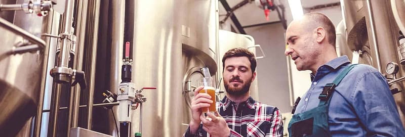 Owner of a brewery with a worker inspecting beer.