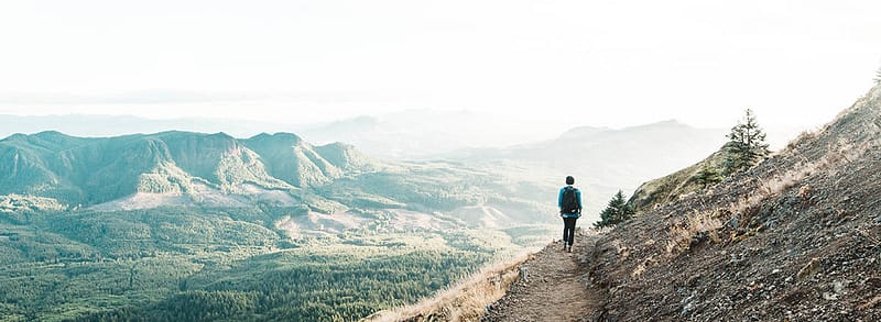 A person with a beanie and a backpack walking on a hiking trail on the cliffside