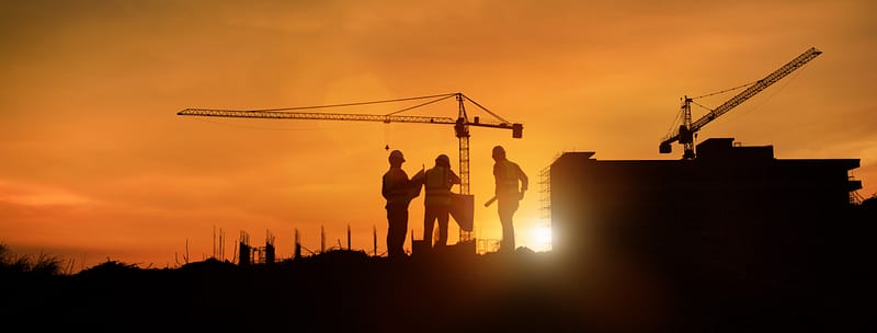 Silhouette of construction site and construction cranes with workers during sunset.