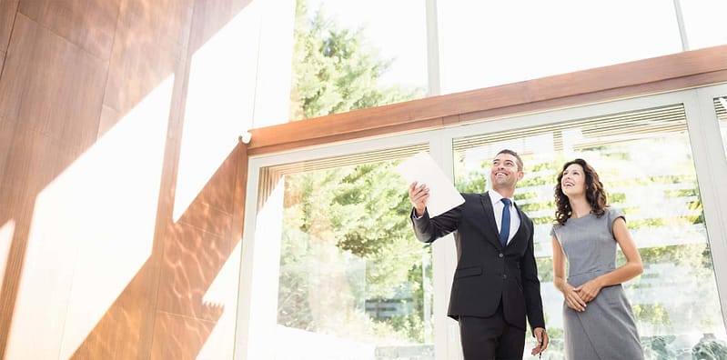 A real estate agent showing a client a house with floor to ceiling windows.