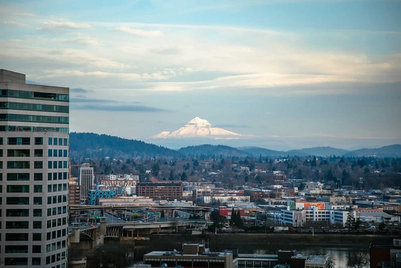Cityscape of Portland, OR with skyscrapers and a mountain view in the background on a partly cloudy day