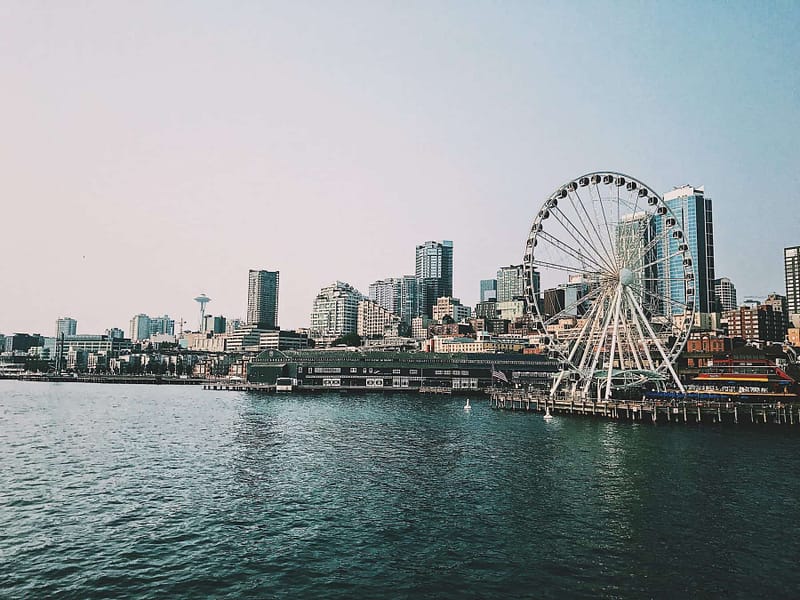 The skyline of Seattle showing the water, space needle in the background, and the Seattle Ferris Wheel. Washington locals should be aware of the new Washington state capital gains tax for individuals who have Washington allocated gains.