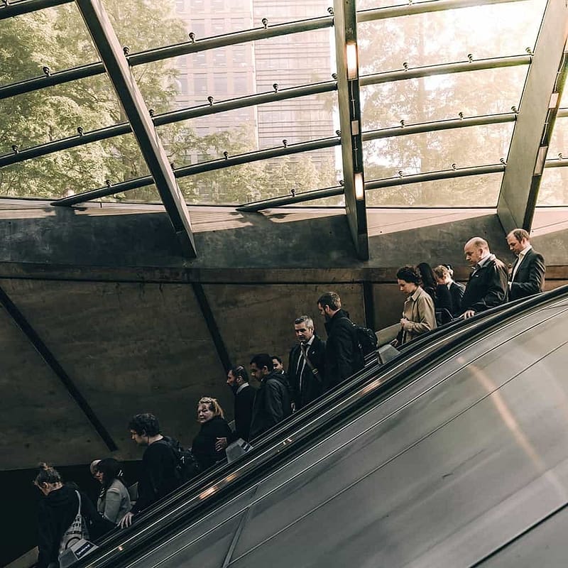 A crowd of people standing on an escalator in a building with a glass ceiling.