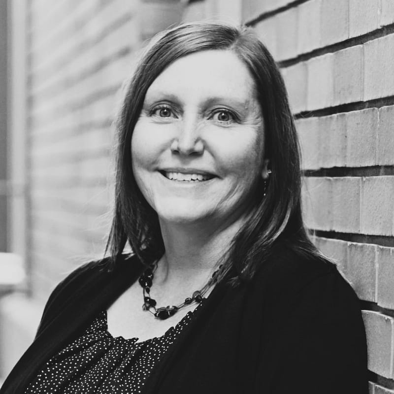 Sheila Savoie's headshot in black and white in front of a brick wall background.