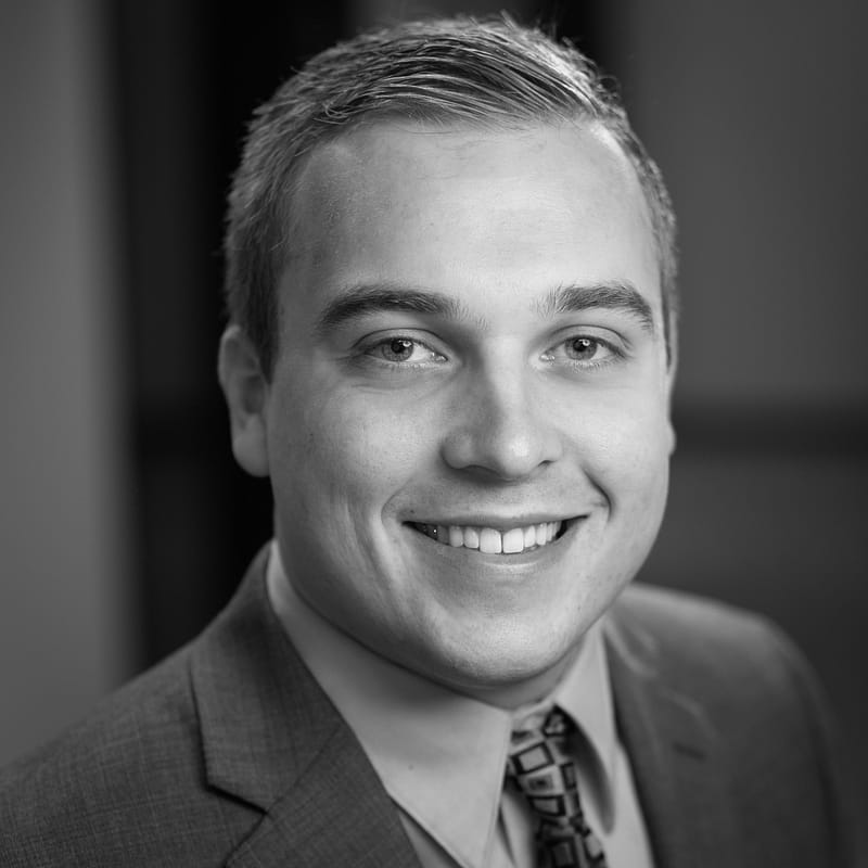 Trent Hardin's headshot in black and white in a blurred office space.